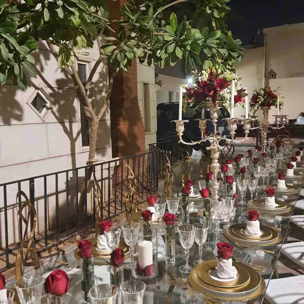 مائدة خارجية بزهور حمراء وشموع وكؤوس